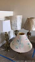 Four brass table lamps together showing varying heights and shades.