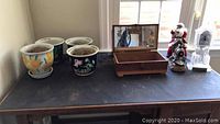 Full view of the lot on a dark table showing four ceramic planter pots, a wooden jewelry box with mirrored lid, white letter box, glass clock with plaque, and Santa figurine on a train.