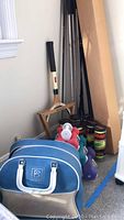 Sports equipment corner with Brunswick bowling ball bag, MacGregor tennis racquet, tennis balls, assorted golf clubs and dumbbell set.