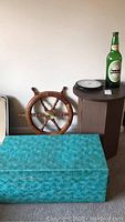 Shot showing ship's wheel, wall clock on table, Heineken bottle, and turquoise trunk