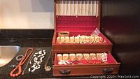 Photo of vintage costume jewelry set displayed on counter and in wooden silverware box with red interior fabric. Shows various earrings, necklaces, rings, and bracelets.