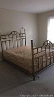 Brass queen bed frame assembled with mattress in a sparsely furnished room, showing the headboard and footboard design and mattress detail