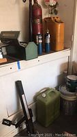Shelf with red vintage fire extinguisher, two blue propane cylinders with propane torch, orange vintage metal gas canister, green metal tool box and a green plastic utility can.