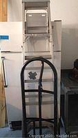 Full view of black rolled steel hand truck in front of metal step ladder inside a storage area.
