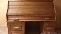 Frontal photo of a wooden roll top desk showing the tambour roll top closed and the drawer layout.