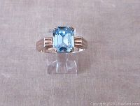 Front view of the ring showing light blue emerald cut stone set in 10K yellow gold filled band.