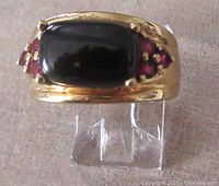 Front view of the ring showing the rectangular black stone and ruby clusters on each side.