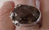 Close-up of the facetted oval smoky quartz stone set east-west in sterling silver with floral motifs.