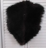 Full view of the triangular black dyed fox fur collar with dark reddish highlights hanging against a white louvered backdrop.