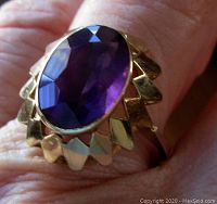 Close-up of vintage gold ring with faceted oval amethyst on finger, showing openwork zigzag design.