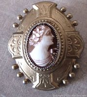Front view of the oval cameo brooch, showing detailed shell cameo carving and engraved gold-tone frame with beads.