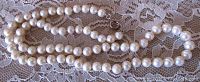 Full view of the single strand cultured freshwater pearl necklace laid out on lace fabric, showing pearl size and clasp.
