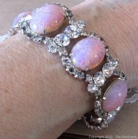 Close-up of bracelet on wrist showing oval iridescent opal glass cabs surrounded by clear rhinestones.
