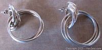 Pair of sterling silver earrings with triple hoops laid flat on a neutral fabric background, showing shape and size.