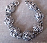 Top side view of silver flower design links showing the open work floral pattern and spring ring clasp.