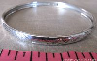 Close-up of the full bangle showing its thin profile and overall engraved design, alongside a pink ruler for scale.