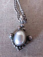 Close-up showing oval cultured pearl pendant with decorative silver accents and chain attachment loop.