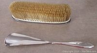 Shoe horn and clothes brush are displayed with bristles and reflective silver surfaces visible, showing overall condition