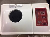 Top view showing white breadmaker with clear lid window and red digital control panel with button labels including delay timer, menu select, and loaf color.