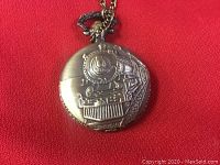 Front cover of pocket watch showing embossed detailed train steam engine design in metal.