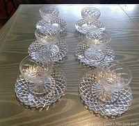 Set of six clear glass footed dessert bowls arranged on matching waffle patterned plates on a wooden surface. The bowls and plates feature a geometric waffle cut design.