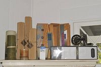 Shelf display with three Mikasa candles, four rolled kraft paper wine bags tied with twine, and a vintage black metal apple peeler with hand crank.