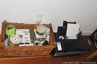 Epson printer next to basket containing office supplies like blank CD spindles, cables.