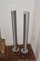 Front view of both silver column speakers with grills attached, cables coiled at base