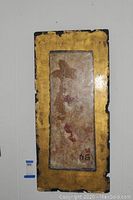 Frontal view of the gold highlighted artwork panel hanging on a white wall showing the overall design and condition.