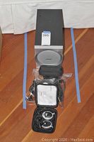 Bose speaker with circular grille, headsets in case, and plastic bags with accessories on hardwood floor.