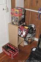 Food waste disposer in unopened box stacked on wooden shelf with other items including kitchen appliances and cardboard boxes