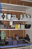 Shelf with various home decor items including candle holders, framed art, tins of candles, and collectible figurines.