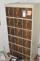 Front view of card file cabinet showing 20 drawers with brass handles and label holders. Cabinet paint is cracked and distressed.