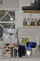 Blue wine glasses, blue glass bowls, white ceramic bowl and plate, metal utensil holder, boxes on shelf below, with glass storage canisters and plates on shelves above.