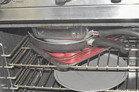 Stacked black and red baking trays and pans inside an oven rack with a round gray pan and glass baking dishes under it