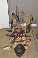 Wood carved rocking horse with painted saddle and black rocker base, large carved wooden Buddha head with textured hair curls, woven baskets including one with a carved and painted mythical creature, rolled rugs on carpeted floor.