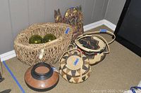 Full lot view showing Indonesian wooden carvings, clay pot, multiple woven baskets, and decorative green balls inside large basket.