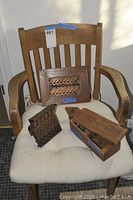 Full view of wood chair with seat cushion holding wooden container and two wood block stamps.