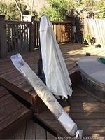 White outdoor umbrella with weighted stand on wooden deck.