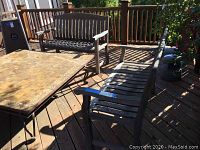 Two wooden outdoor patio benches on a wooden deck with wide armrests and slatted seats and backs. Show heavy wear and weathering.
