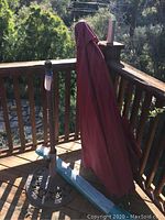 Full view of outdoor umbrella draped in red fabric cover and cast metal umbrella base on wooden porch deck.