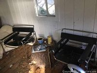 Two imitation Wassily chairs placed on a wooden floor with visible wear and dirt. Shows overall condition and surroundings.