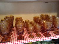 Wide shot showing multiple amber glass goblets of different sizes arranged on a red and white checkered surface against a wall.