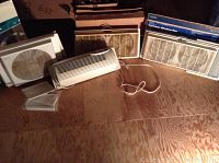 Four portable window fans placed on wooden floor in attic environment, showing front protective grilles and power cords.