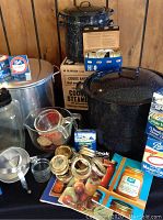 Photo showing large enamel canning pot with lid, measuring cup, mason jar lids, rings, and three canning books.