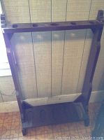 Wooden gun rack with dark stain and cutouts for holding five guns vertically, standing on floor against wall.