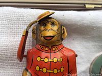 Close-up of the mechanical monkey tin bank, showing detailed painted features and tipping hat worn by monkey dressed in a red uniform.