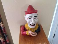 Front view of the cast iron clown mechanical bank showing the clown bust with red hat and colorful paint