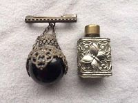 Miniature perfume bottle brooch with dark red/black glass orb and silver filigree, alongside a small ornate silver-tone metal Western Germany perfume bottle.