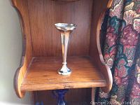 Tall slender sterling silver vase displayed on a wooden shelf.